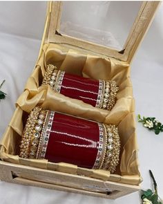 two red bracelets in a wooden box on a white cloth covered table with flowers