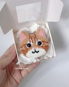 a hand holding an open box with a crocheted cat face on the inside