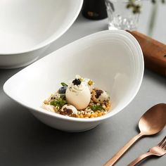 a white bowl filled with food on top of a table next to utensils