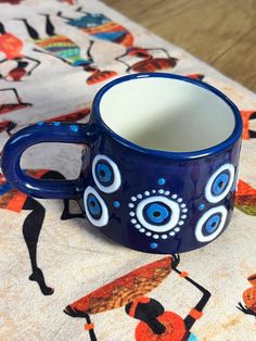 a blue coffee cup sitting on top of a colorful table cloth with an eyeball design