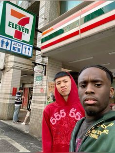 two young men standing in front of a seven eleven store on the corner of a city street