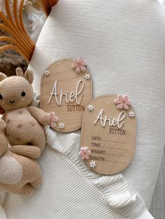 a teddy bear sitting on top of a white blanket next to two wooden tags with names