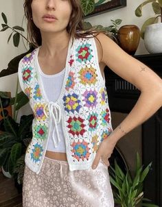 a woman standing next to a potted plant wearing a white top and colorful vest