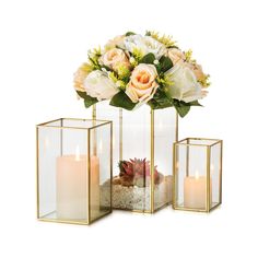 three glass vases with flowers and candles in them on a white surface, one is filled with sand