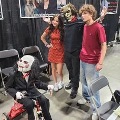 three people posing for a photo with a creepy clown on a tricycle in front of them