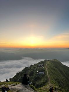 people sitting on top of a mountain watching the sun rise over foggy hills and valleys