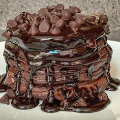 a large stack of chocolate cake on top of a white plate covered in melted chocolate