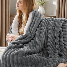 a woman sitting on a bed wrapped in a gray blanket