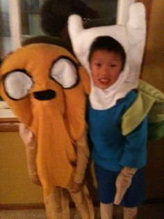 a young boy standing next to a stuffed animal with eyes on it's face