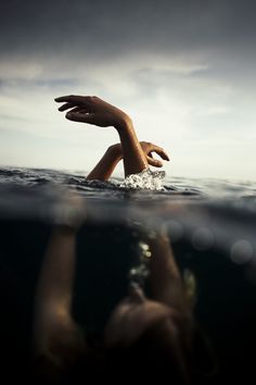 someone is swimming in the ocean with their hand up to the water's surface