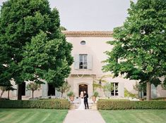 a bride and groom standing in front of a large house with trees on either side