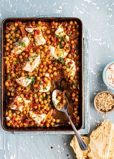 a pan filled with baked chickpeas next to bread and seasoning on the side