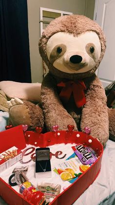 a stuffed slotty bear sitting on top of a bed next to a red suitcase