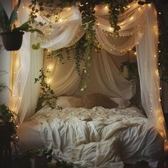 an unmade bed with white sheets and fairy lights on the headboard is surrounded by greenery