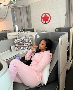 a woman in pink is sitting on an airplane and talking on her cell phone while holding a purse