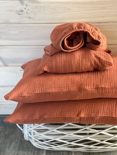 an orange blanket is stacked on top of a white wicker basket with two pillows