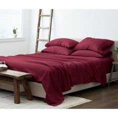 a bed with red sheets and pillows in a white room next to a wooden ladder