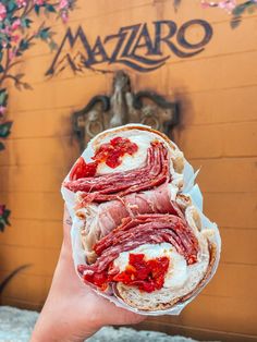 a person holding up a sandwich with meat and cheese on it in front of a building