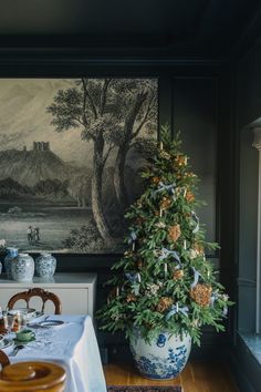 a decorated christmas tree sitting in front of a painting on the wall next to a dining room table