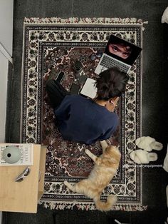 a woman sitting on top of a rug next to an orange and white cat near a laptop computer