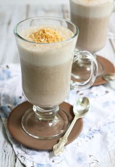 two glasses filled with food sitting on top of a wooden table next to spoons