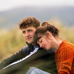 a man and woman sitting next to each other on top of a grass covered field