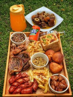 a wooden tray filled with meats and other foods on top of a grass covered field