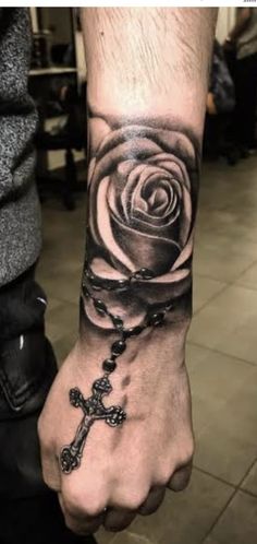 a man's arm with a cross and rose tattoo on the wrist that is black and white