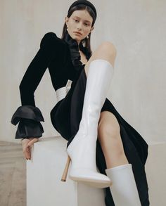 a woman sitting on top of a white block with her legs crossed and wearing high heel boots