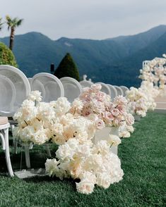 rows of white chairs with flowers on them in front of mountains and greenery at an outdoor wedding ceremony