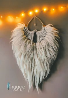 a white feathered heart hanging on a wall with string lights behind it and the words hugge written above it