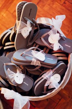 several pairs of flip flops with bows in a basket on a wooden floor,