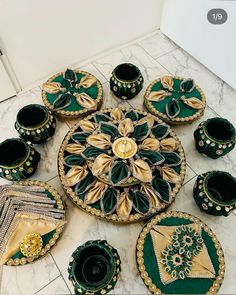 a table topped with lots of green and gold plates on top of a marble floor