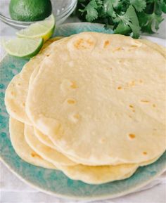 three tortillas on a plate with limes and cilantro in the background