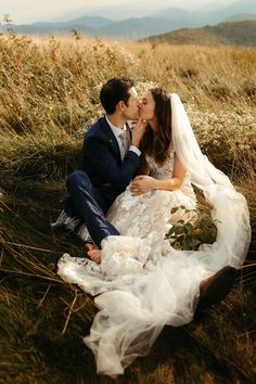 a bride and groom sitting in the grass kissing