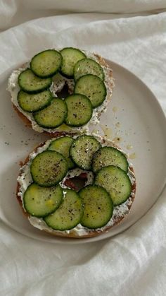 two pieces of bread with cucumbers on them sitting on a plate next to each other