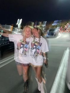 two women standing next to each other in front of a parking lot at night with their arms around each other