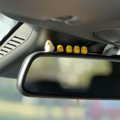 three little yellow chicks sitting on the dash board of a car in front of a rear view mirror