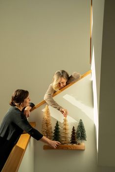 two women are looking at some miniature trees on the wall