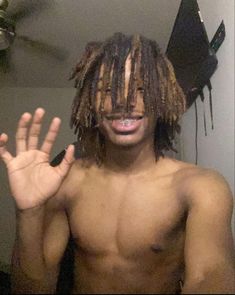 a shirtless man with dreadlocks holding his hand up in front of him