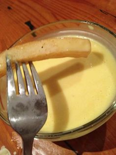 a glass bowl filled with yellow liquid and a silver fork on top of it next to a wooden table