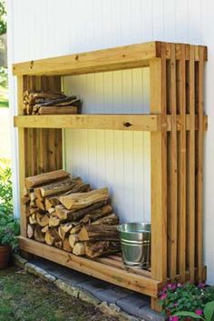 a wooden shelf filled with firewood next to a white building and flower pots on the ground