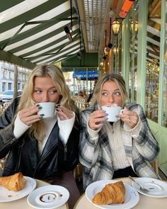 two women sitting at a table drinking coffee and croissants