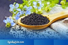 a wooden spoon filled with black seed on top of a table next to blue flowers