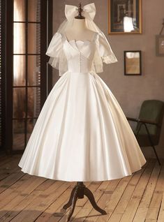 a white wedding dress on display in a room with wooden flooring and framed pictures