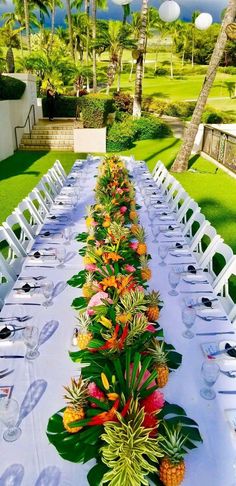 a long table is set with pineapples and tropical flowers for an outdoor dinner