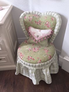 a green chair with pink flowers on it next to a white dresser and drawers in a room