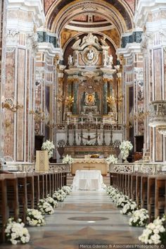 the interior of a church with pews and white flowers on the aisle, along with an altar