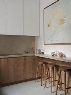 an image of a kitchen setting with bar stools and art on the wall behind it