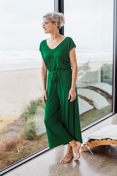 Tired of coordinating tops and bottoms? The Kiova Jumpsuit takes the guesswork out of getting dressed and makes it fun again. The jumpsuit top is a relaxed V-Neck and V-Back with a cap sleeve, connected to a wide leg pant by an elastic waistband with an adjustable drawstring. Did we mention it has pockets? Try one today and let the fun begin. Green V-neck Jumpsuit For Loungewear, Green V-neck Casual Jumpsuits And Rompers, Men's Bedding, Wrap Jacket, Getting Dressed, Eco Friendly Clothing, Sleeveless Tunic, Wide Leg Pant, Womens Size Chart